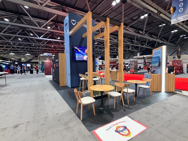 Peregrine booth at FRI 2026 showing the open seating area under the wood pergola, with fire trucks in the background
