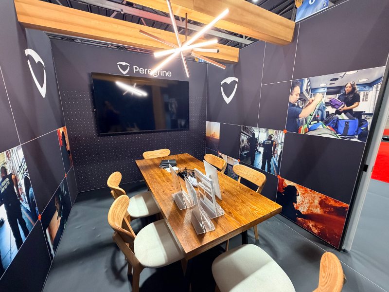 Peregrine's private conference room inside the FRI 2026 booth, with a wood table, mid-century chairs, and a starburst LED light