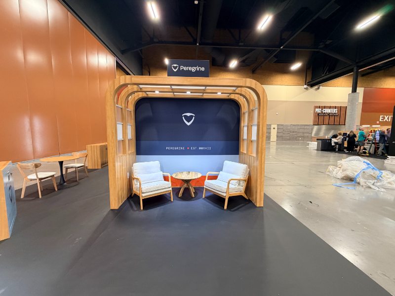 Curved wood lounge nook with two armchairs inside the Peregrine booth at NRTCCA 2026